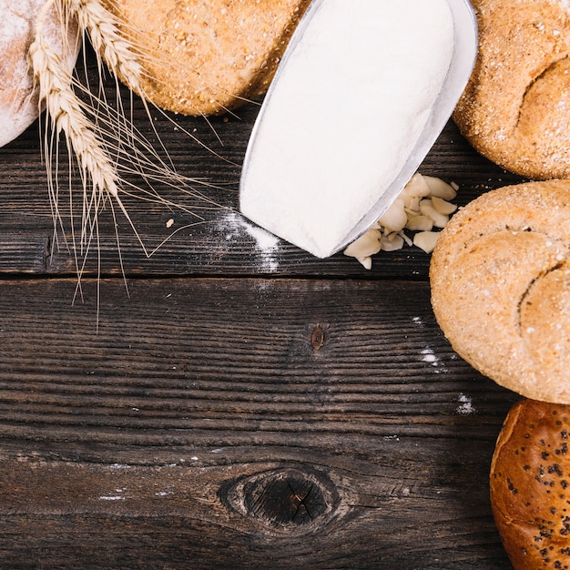 Flour in shovel with baked breads on wooden textured background