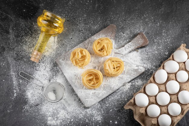 Flour spilled on wooden board, raw eggs and oil on black surface