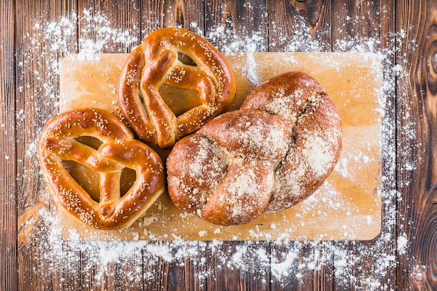 播種したパンの上に小麦粉を広げ、木製のテーブル上のチョッピングボードでプレッツェル