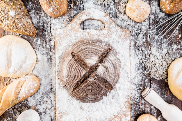 Flour spreads over the different types of bread loaves on the wooden table