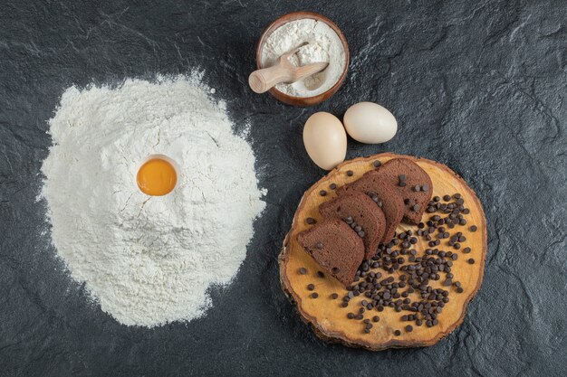 Flour with egg yolk, eggs and cake slices on dark surface. 