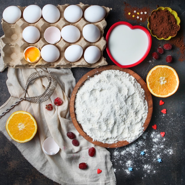 Flour with eggs, orange, milk, cocoa, whisk in a bowl on stone surface