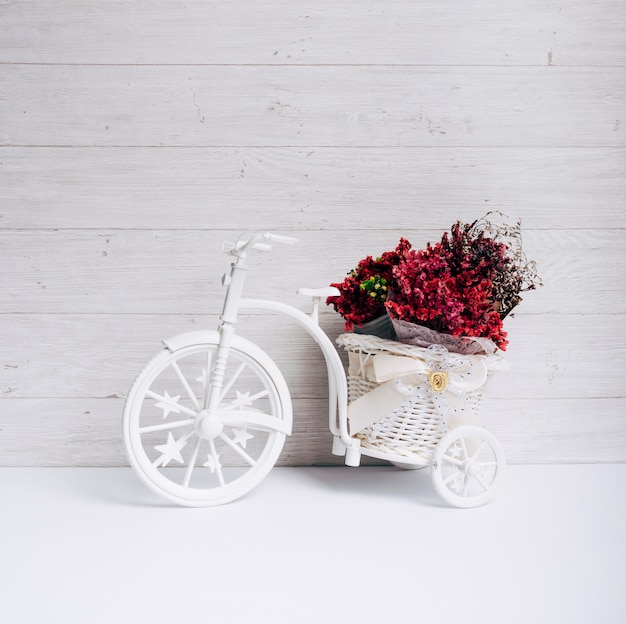 Flower basket in the white bicycle on desk against wooden wall