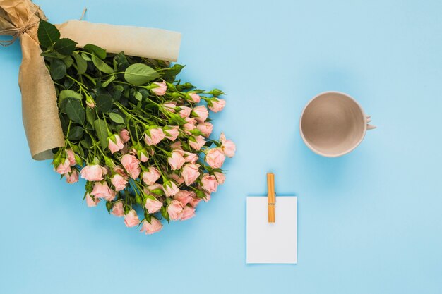 Букет цветов; карточка и пустая чашка на синем фоне