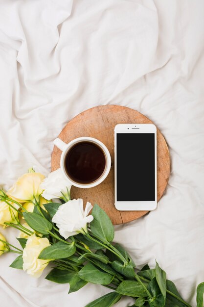 コーヒーカップとベッドの上の携帯電話と花の花束