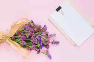 Free photo flower bouquet wrapped in brown paper near the white blank paper on clipboard