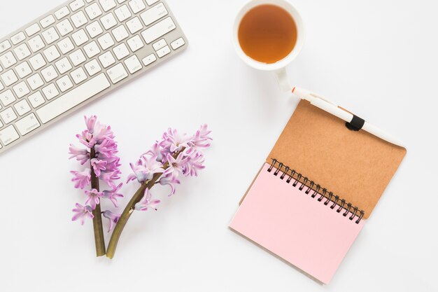 Flower branches with notebook, keyboard and tea cup