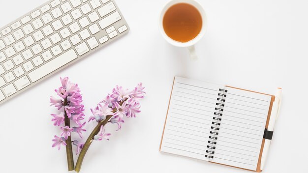 Flower branches with notebook, keyboard and tea 