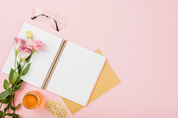 Flower on an open notebook; eyeglasses; juice jar and muesli on pink background