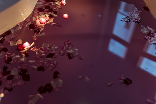 Flower petals on water near burning candles in spa tub 