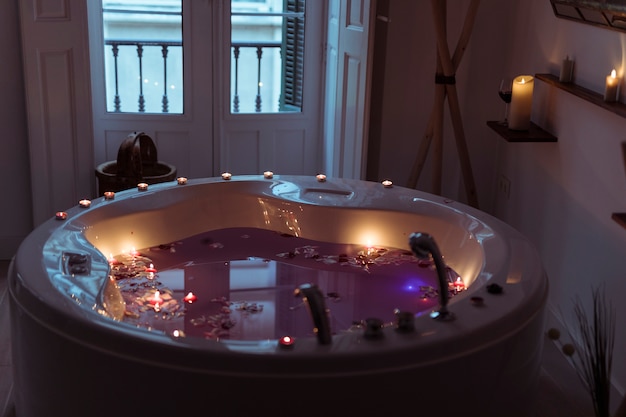 Flower petals on water in spa tub with burning candles on edges 