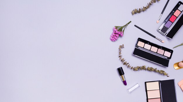 花と口紅の小枝。化粧用ブラシ;口紅;紫色の背景にコンパクトパウダーとアイシャドウパレット