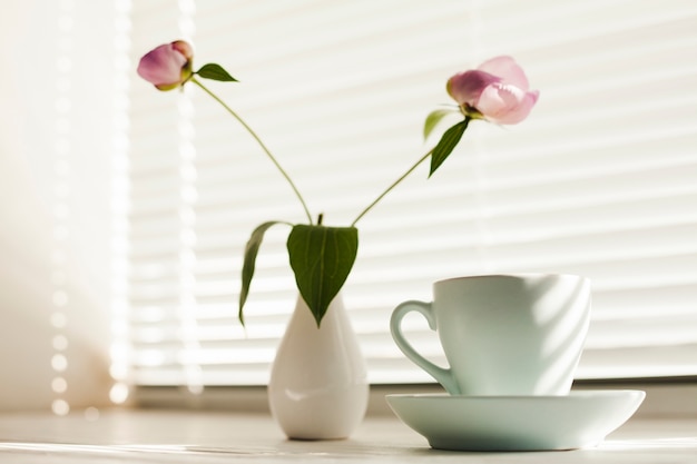 블라인드 근처 접시와 꽃 vas와 커피 컵