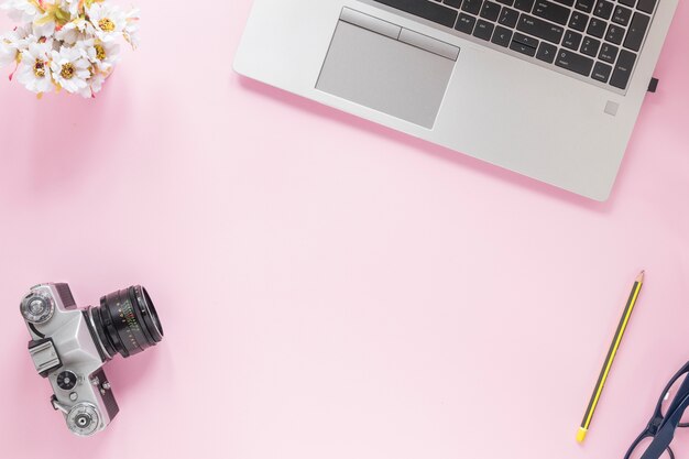 Flower vase; camera; pencil; eyeglasses and laptop on pink background