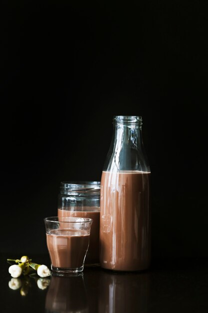 Flower with chocolate milkshake in bottle; glass and jar on black background