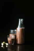 Бесплатное фото Цветок с шоколадным молочным коктейлем в бутылке; стекло и банку на черном фоне