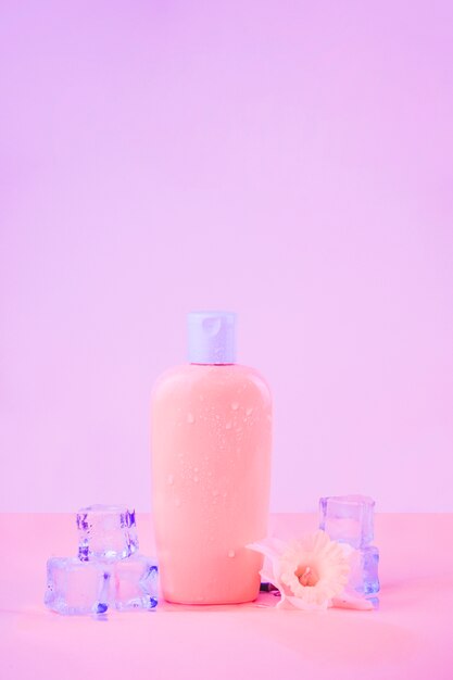 Flower with crystal ice cubes with sunscreen bottle against pink backdrop