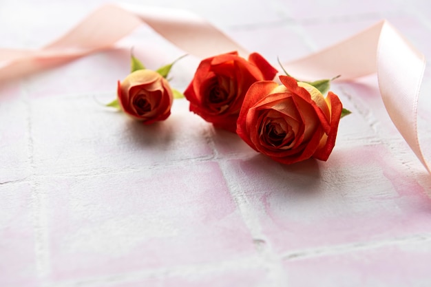 핑크 타일 배경에 빨간 장미와 꽃잎으로 만든 꽃 구성 프레임