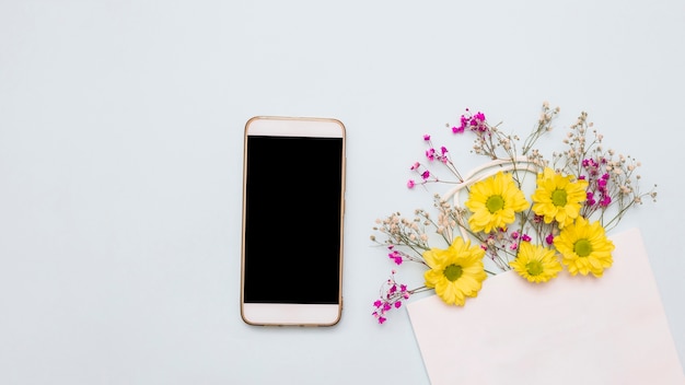 Free photo flowers decorated paper bag and smartphone on white backdrop