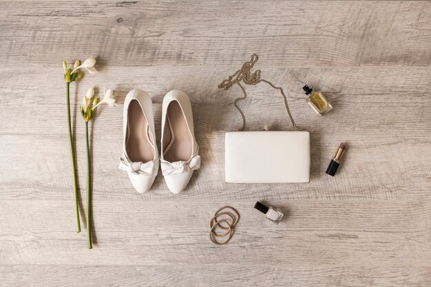 Flowers; dress shoes; clutch; perfume; lipstick; nail varnish and hairbands on wooden backdrop