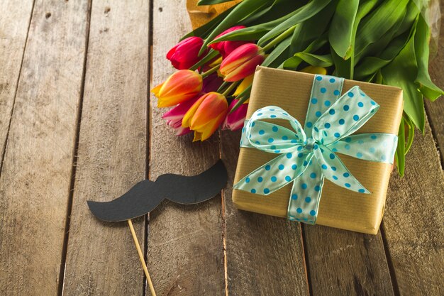 Flowers, mustache and gift on wooden surface for father's day