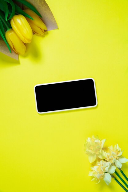 Flowers and phone. Monochrome stylish and trendy composition in yellow color on  background. Top view, flat lay. Pure beauty of usual things around. Copyspace for ad. Holiday, food, fashion.