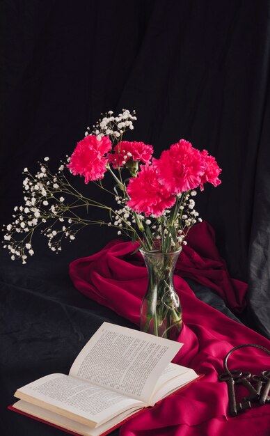 Flowers with bloom twigs in vase near volume and keys on pink textile in darkness