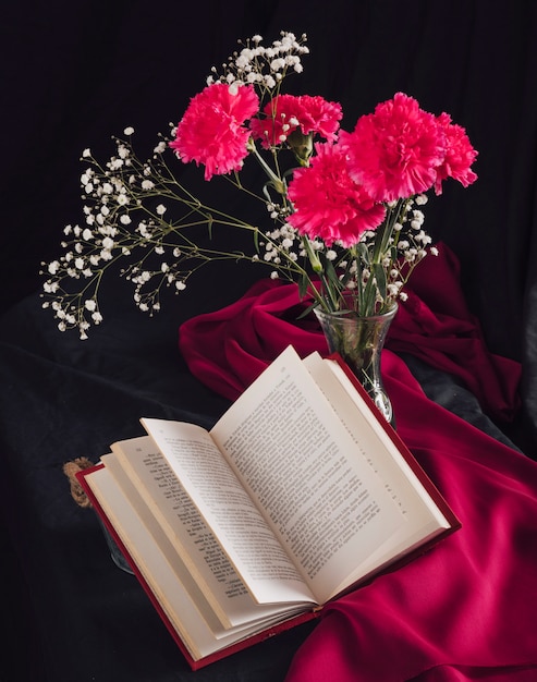 Flowers with bloom twigs in vase near volume and rose textile in darkness