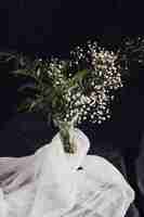 Free photo flowers with plants in vase near white textile and beads