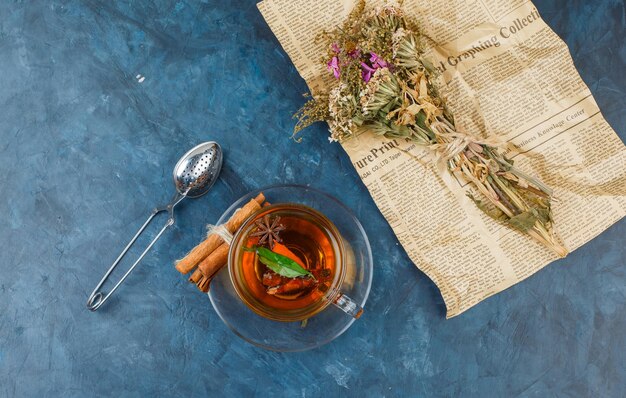 Flowers wrapped in newspaper with a cup of tea,cinnamon and a tea strainer