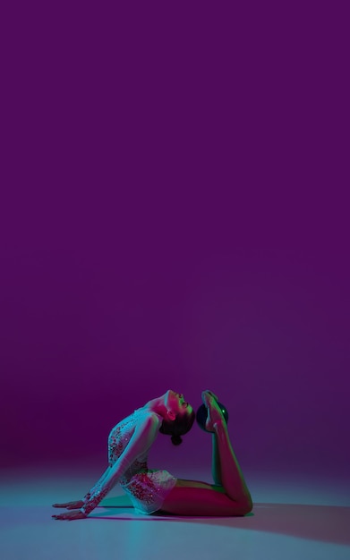 Free photo flyer. young female athlete, rhythmic gymnastics artist dancing, training with tape isolated on purple studio background in neon light. beautiful girl practicing with equipment. grace in performance.