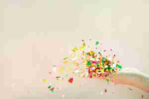 Free photo flying colorful confetti from hand on beige background