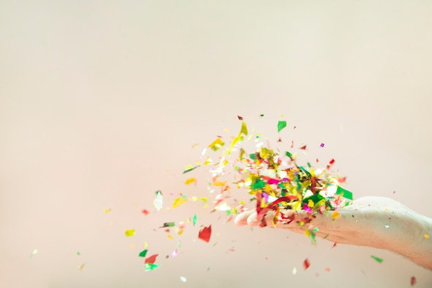 Flying colorful confetti from hand on beige background