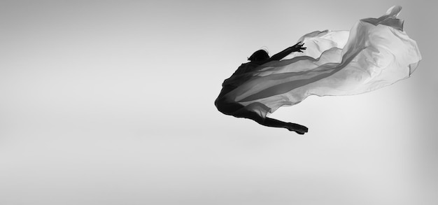 Flying high Professional ballering dancing with transparent veil making movements in a jump Black and white