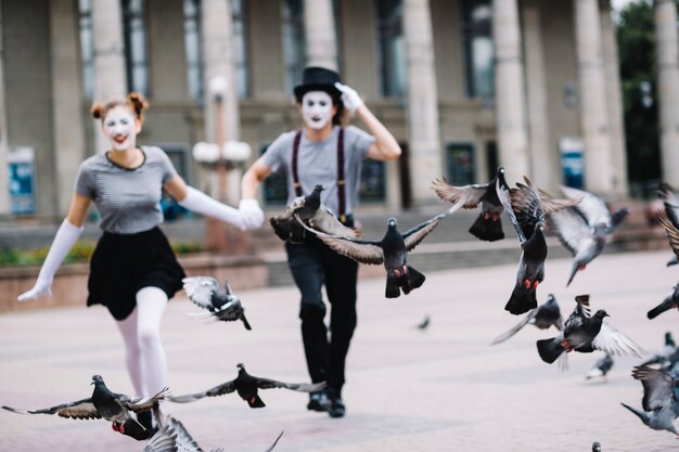 Flying pigeons near running mime couple