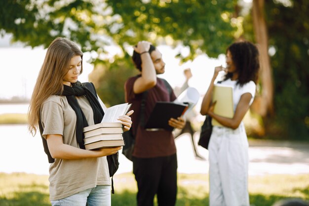 別々に立っている白人の女の子に焦点を当てます。大学の公園で一緒に立っている留学生のグループ