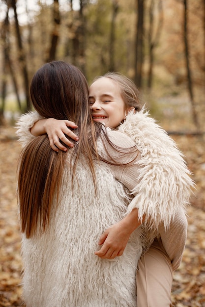 Focus on a little girl hugging her mother. Brunette woman hugging her daughter. Girl wearing beige sweater and mother wearing white clothes.