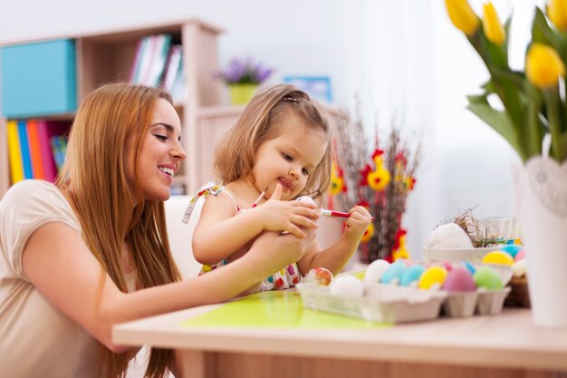 Focus little girl painting easter eggs with mother