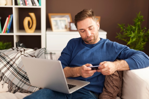 Mettere a fuoco l'uomo utilizzando il telefono cellulare e il laptop a casa