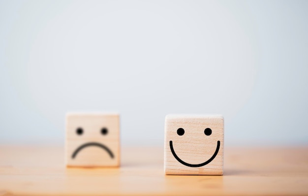 Фокус улыбающегося лица и расфокусировка грустного лица на кубе из деревянного блока для концепции выбора позитивного мышления.