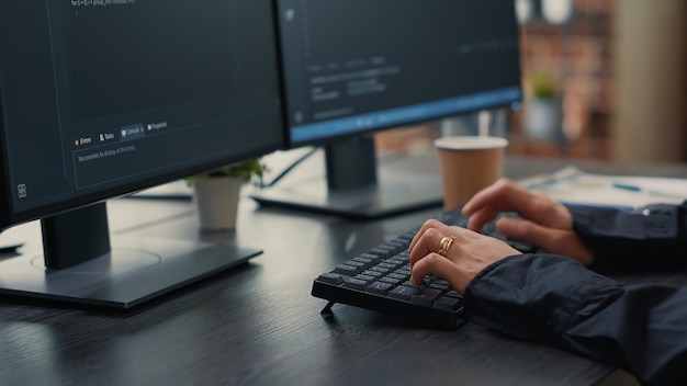 Focus on software developer hands typing source code on keyboard while looking at computer screens with programming interface. Programer sitting at desk with clipboard writing algorithm.