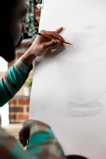 Foto gratuita artista afroamericano concentrato che disegna un vaso con la matita su tela, ragazzo nero seduto al cavalletto che impara a disegnare durante il laboratorio d'arte, imparando nuove abilità creative. hobby per alleviare lo stress