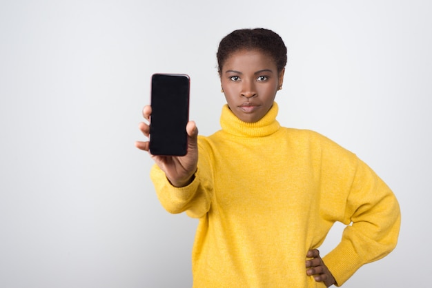 空白の画面を持つ携帯電話を示すアフリカ系アメリカ人の女性に焦点を当てた