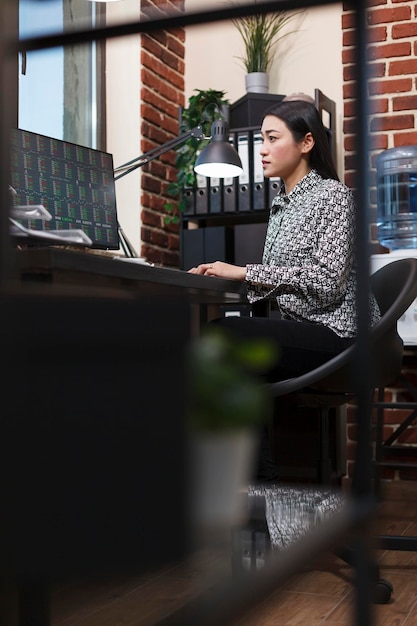 Focused asian marketing agency office worker using work computer to analyze financial market data. Company employee reviewing organization market value and analyzing finances.