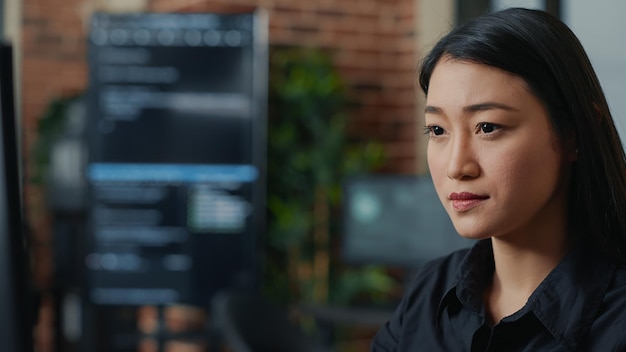 Free photo focused asian software developer writing programming code and smiling sitting at desk in database development agency. friendly coder computing big data casually in it startup office.