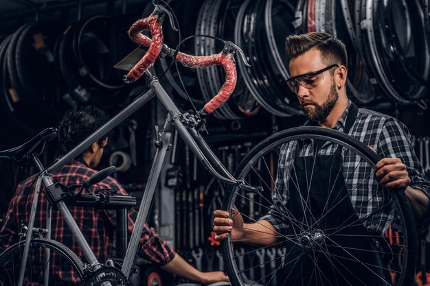 眼鏡をかけた魅力的な男性は、忙しいワークショップで自転車用のチェーンホイールです。