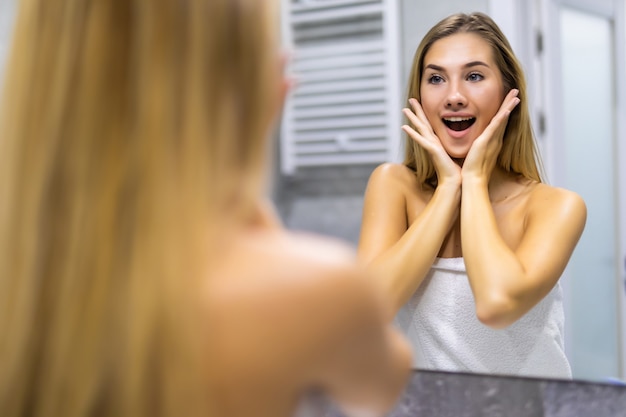 Bella giovane donna concentrata che si guarda nello specchio del bagno a casa