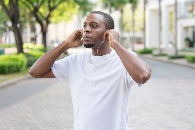 Focused black guy in sports tshirt fixing earphones before morning run.