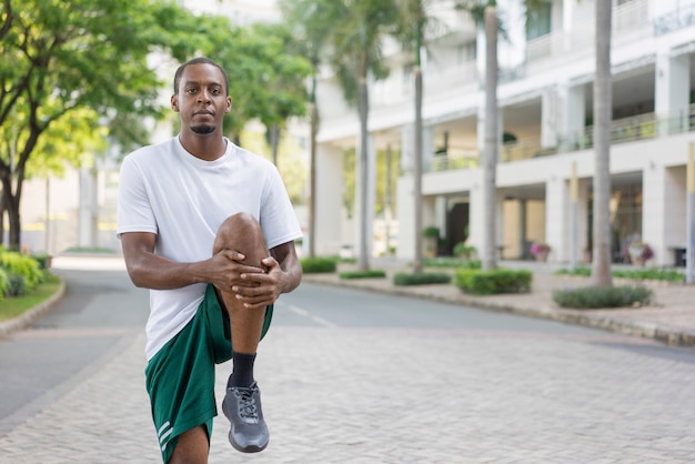 Focused black sportsman warming up legs before training.