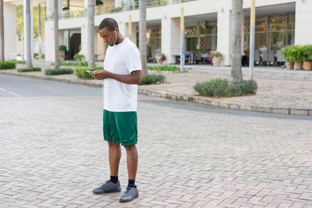 Сосредоточенный черный турист готовится к бегу и настройке плейлиста по телефону.